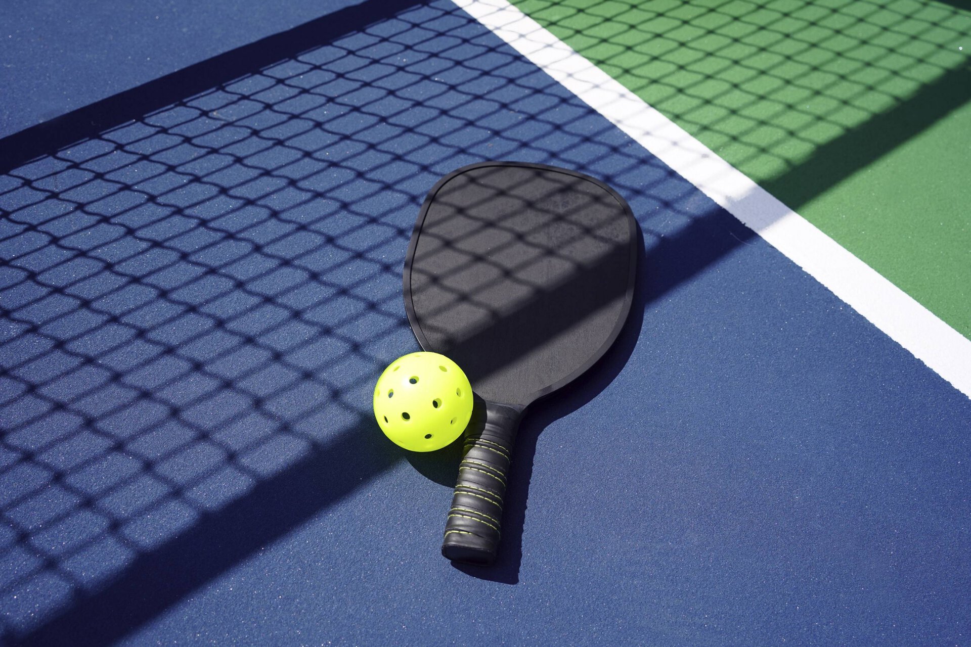 closeup of a pickleball paddle and ball on a pickleball court