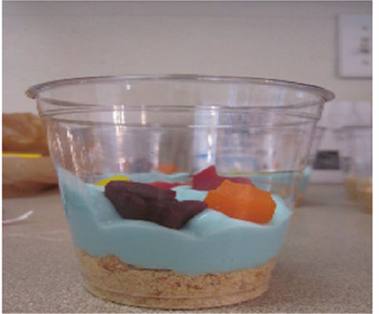 clear cup with crushed graham crackers on the bottom, topped with blue tinted whip cream and candy fish