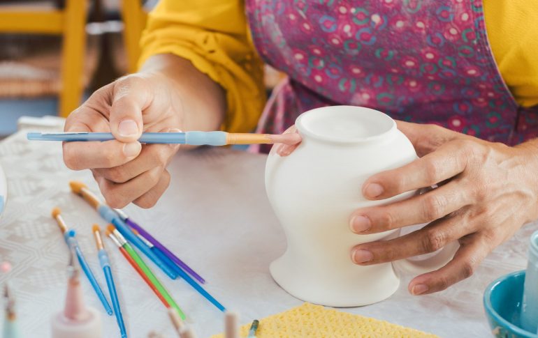 hands holding a paintbrush and painting a ceramic vase