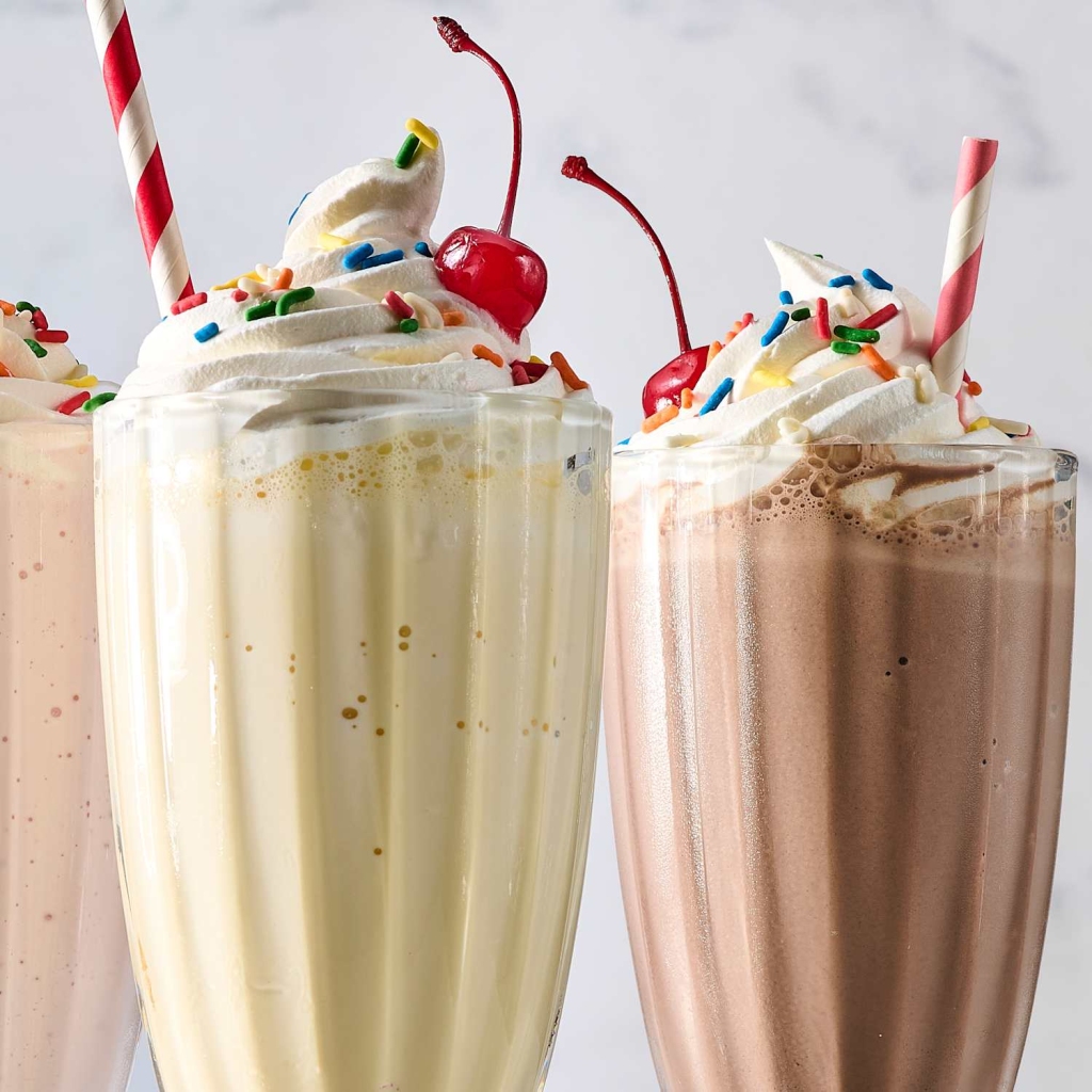3 milk shakes in tall glasses - strawberry, vanilla and chocolate, each with whip cream and a cherry and a straw