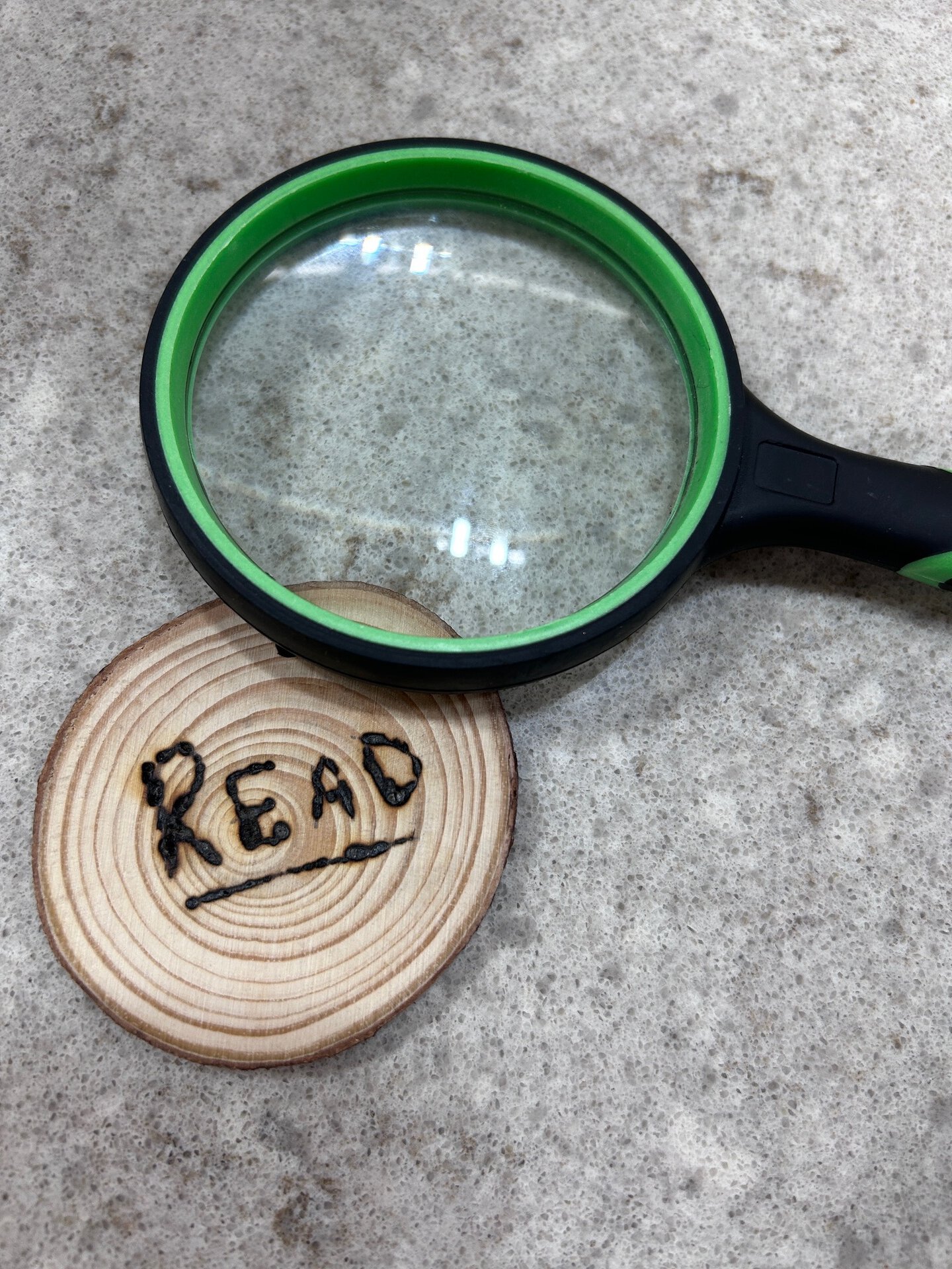 A circular piece of wood with "READ" burned onto it and a magnifying class lying beside it.