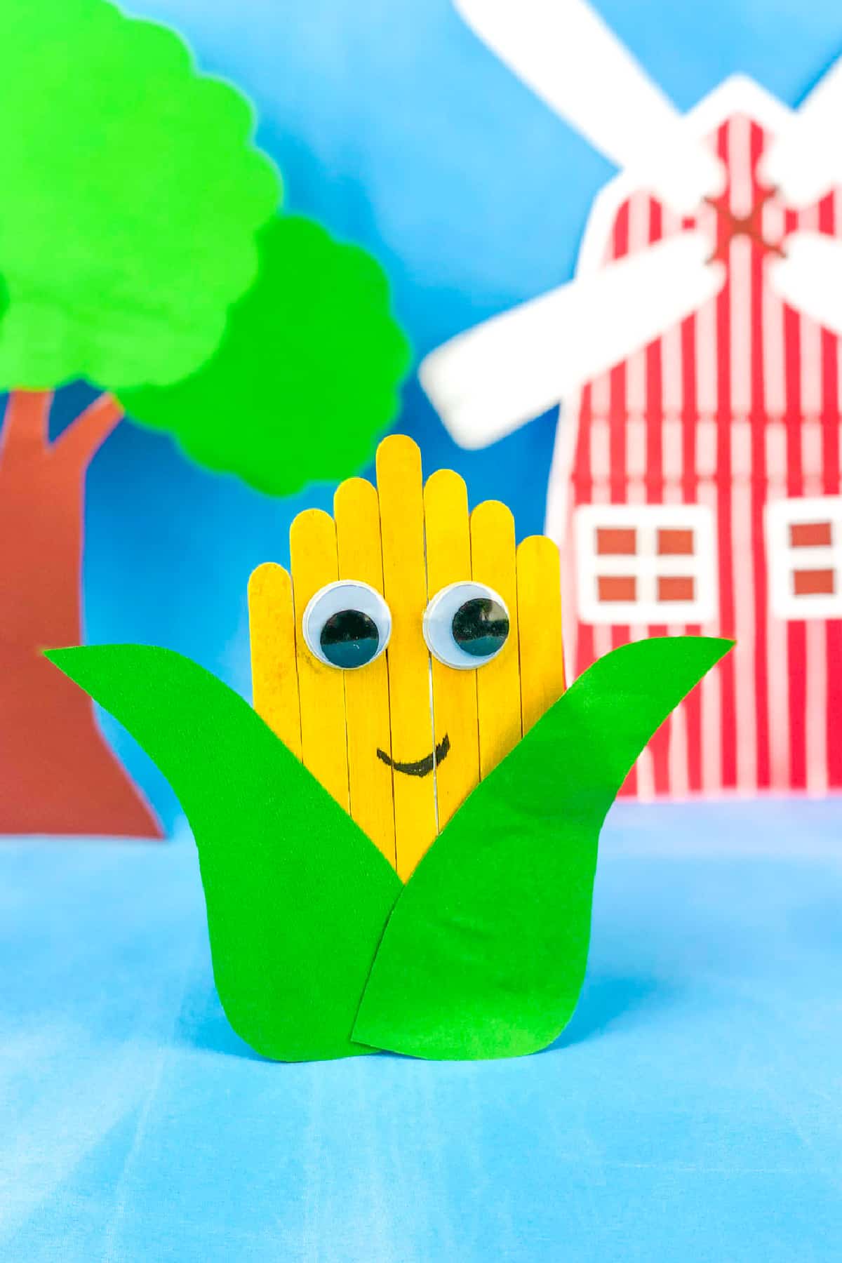 craft sticks painted yellow and glued side by side to resemble a corn cob with googly eyes. Green construction paper is cut to look like leaves and glued on the cob