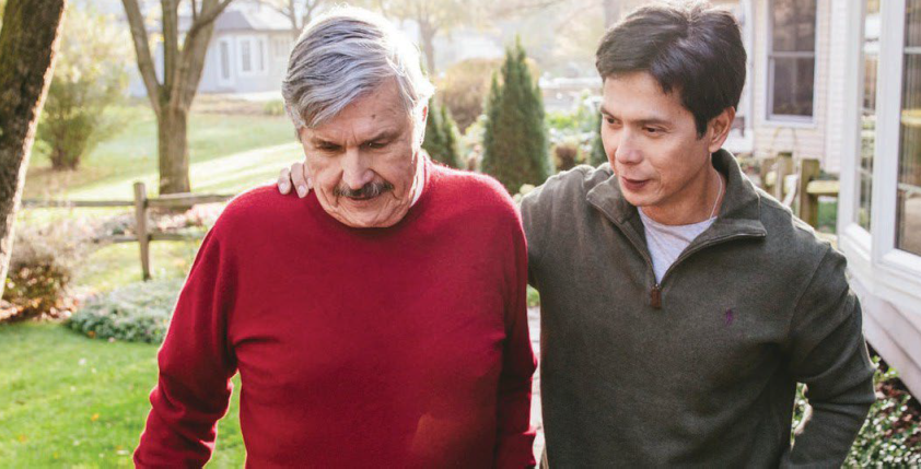 A younger man with his hand on the shoulder of an older man walking outside