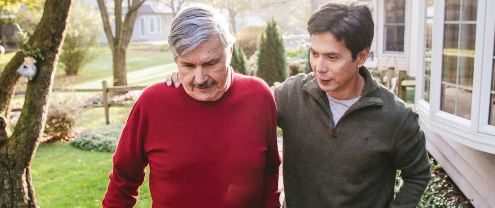 A younger man with his hand on the shoulder of an older man walking outside