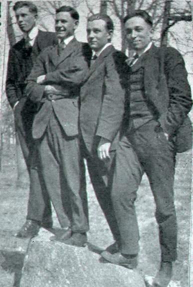 old photo of 4 young men dressed up and standing on a boulder outside